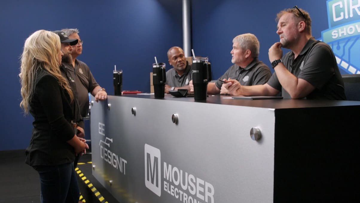 Circuit Showdown scene featuring show hosts convening at the judges table to deliberate with blue walls and branded logos behind them